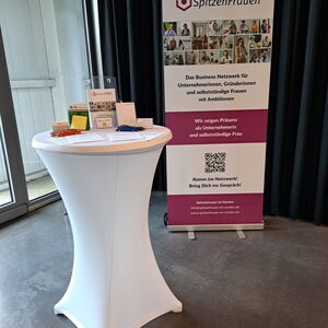 Bild vom Messestand mit Rollup und Stehtisch mit Werbemitteln.